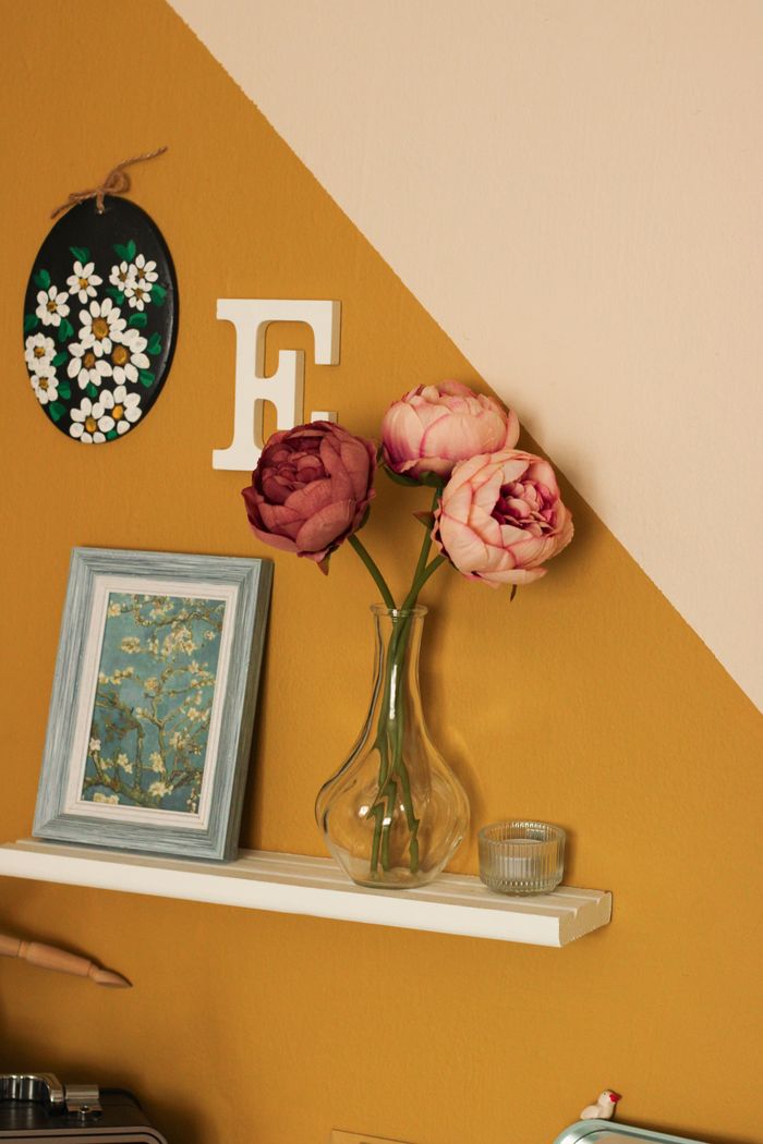 gallery-01 Aesthetic home decor with peonies in glass vase against a vintage yellow backdrop.