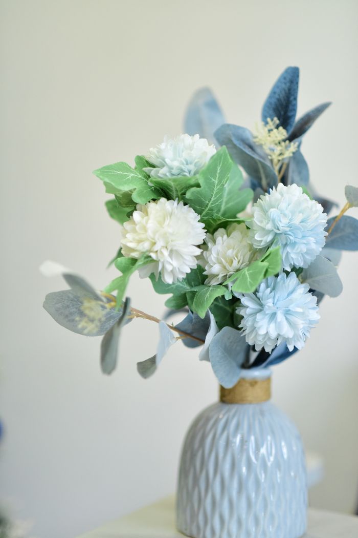 services-01 Delicate blue and white artificial flowers arranged in a textured ceramic vase indoors.