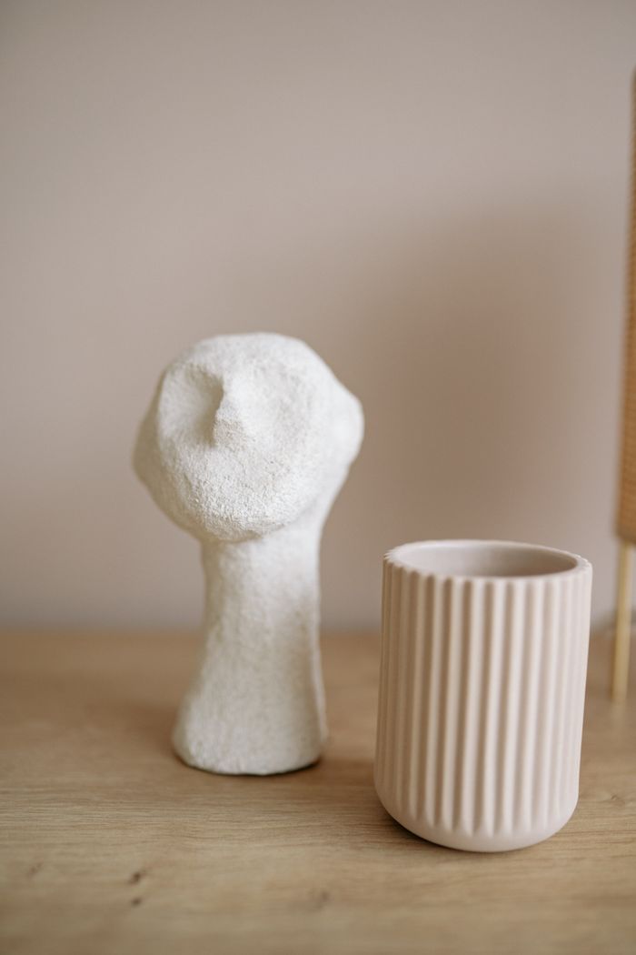 A simple composition of a ceramic figurine and a textured vase on a wooden surface.