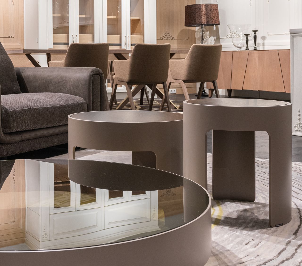 gallery-02 Small round tables placed near sofa and and sat of brown chairs at wooden cupboard with lamp and candlestick in modern apartment